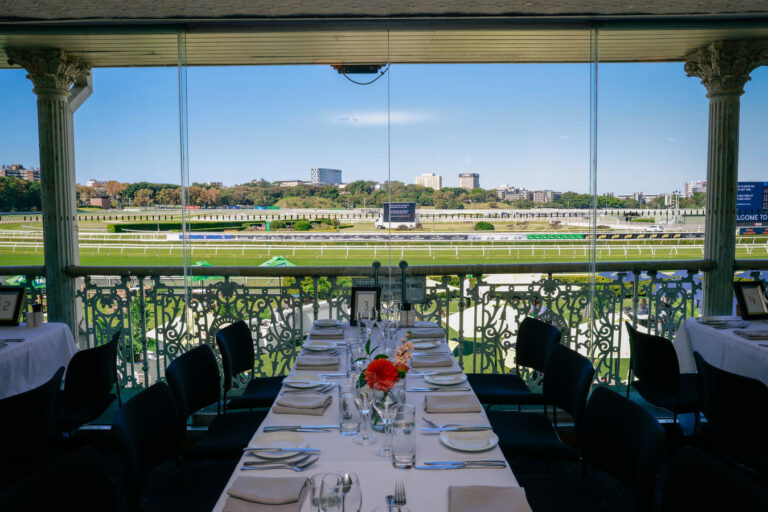 Empty tables at a restaurant within a racecourse grandstand, with the track visible outside