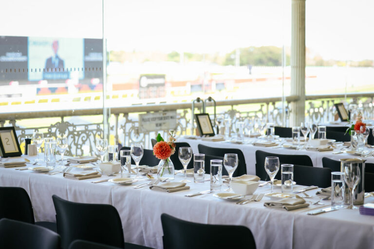 Empty tables at a restaurant within a racecourse grandstand, with the track visible outside