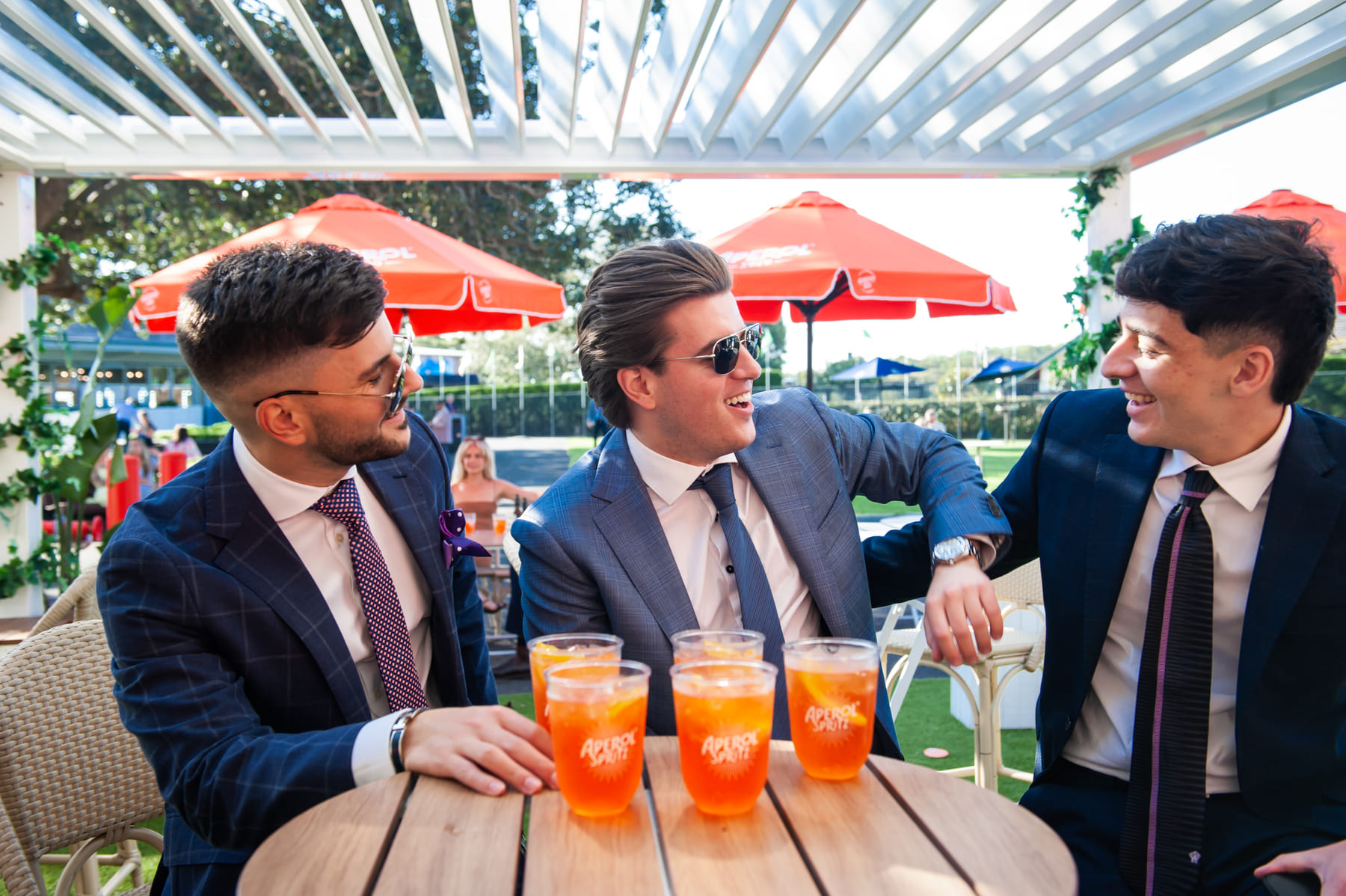 A group of suited racegoers chat over glasses of Aperol Spritz in an outdoor area at Royal Randwick.