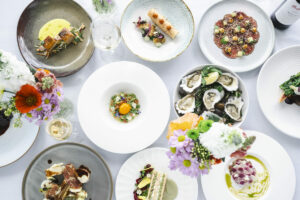 A flat lay of assorted savoury dishes is shown with flowers on a table.