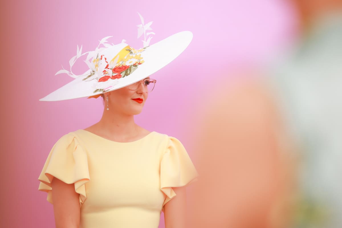 A female racegoer poses against a pastel background.